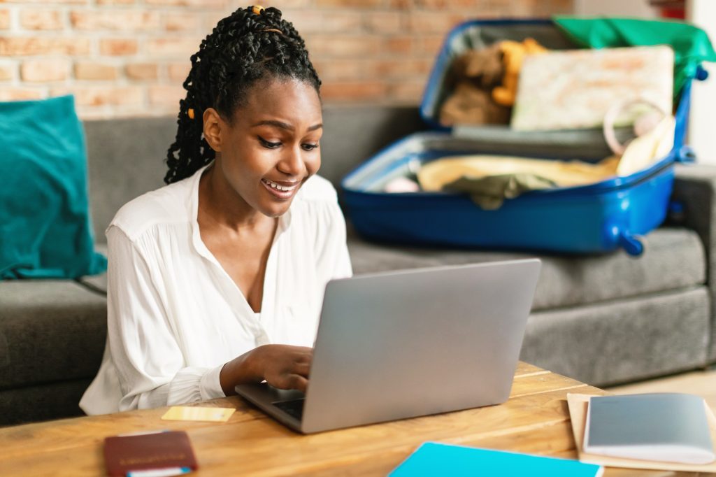 African american woman planning vacation travel with laptop, reading tourist blog online or booking